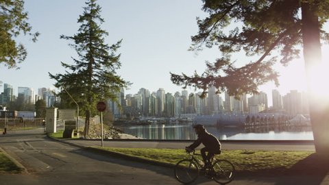 Dolly shot of Vancouver skyline with park, ocean, boats, and cyclist.
