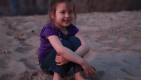 A small child sitting on the sand at sunset.