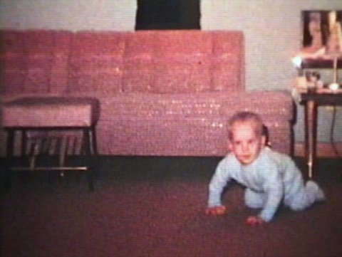 A cute little baby wearing a blue sleeper practices crawling and then plays with a stuffed Panda bear. (Vintage 8mm film)