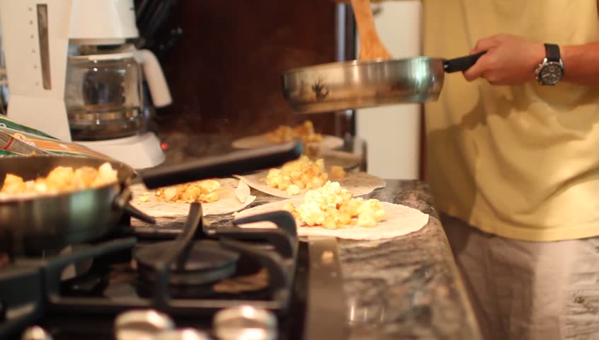 Burritos, Breakfast, Cooking, Eggs, Potatoes. The scene focuses on fresh homemade breakfast. Breakfast burritos are being made with eggs and tater tots while coffee brews in the background.