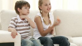 Footage in high definition of little boy and girl on sofa eating and watching television 