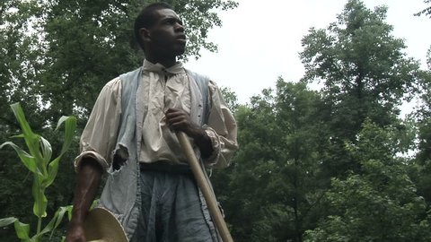 VIRGINIA - 2011.  Re-enactment, recreation of young African-American black man Slave circa 17th and 18th century southern United States.  Slavery reenactment of work on farm or tobacco plantation.