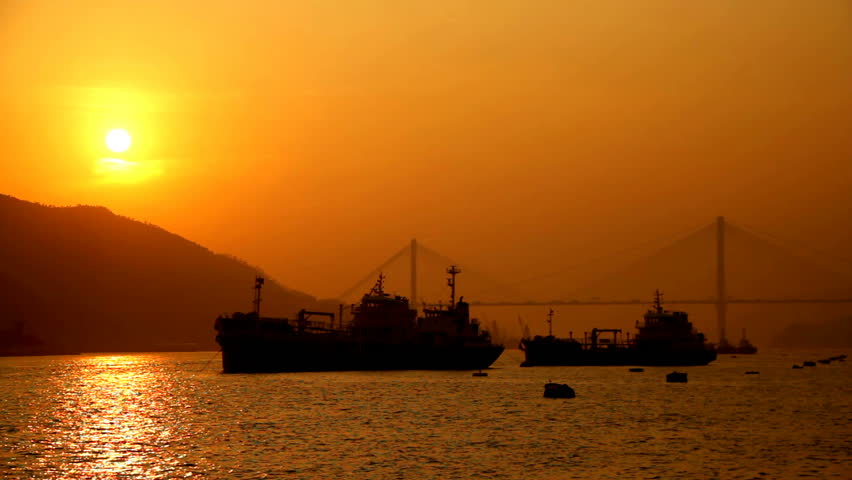 Hong Kong Sunset Cityscape over Sea. Sunset scene with mountain and sun at the left, ships at the middle and a bridge at the back at right side.