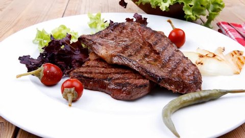 meat food : two grilled steak on green lettuce salad with roast onion and red hot chili peppers on dish over wooden table 1920x1080 intro motion slow hidef hd