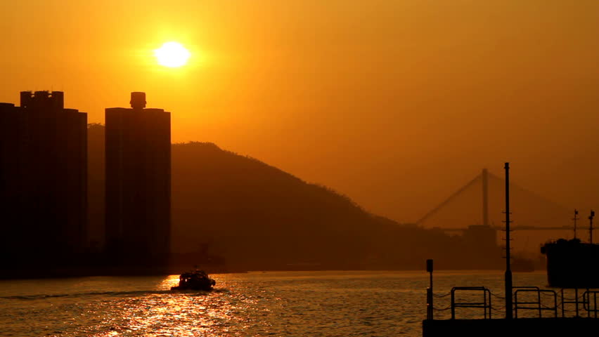 Hong Kong Sunset Cityscape over Sea. Sunset scene with high rise apartment buildings at the left and pier at the right. Golden sunshine reflection on sea. 