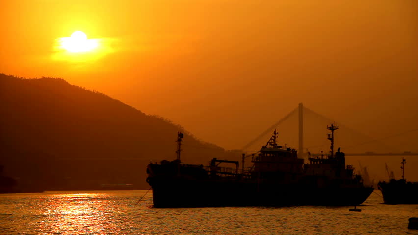 Hong Kong Sunset Cityscape over Sea. Sunset scene with mountain and sun at the left, ships at the middle and a bridge at the back at right side.