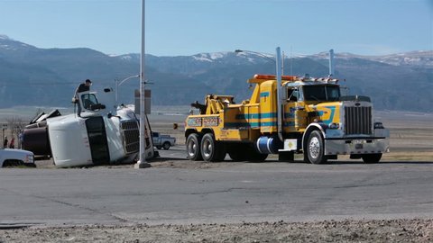 MORONI, UTAH - MAR 2014: Accident truck trailer rollover tow truck helps. Rural community State highway corner a careless professional semi truck driver speeds and rolls his tractor trailer rig.