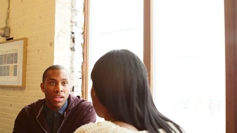 Over the shoulder shot of a man talking to a woman while on a date in a cafe drinking coffee, with slight camera movement