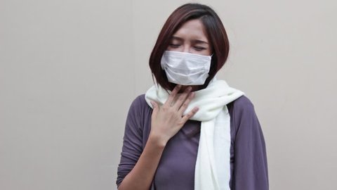 sick woman with hygiene mask suffers from sore throat problem or cold