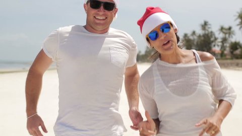 Funny happy couple fooling around in santa hats on the beach
