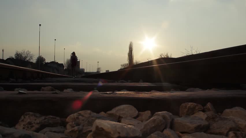 Silhouette of young pretty girl walking on the railway track. Beautiful girl in the red dress walking on the railroad tracks, passing over the camera, medium shot, long shot, abstract, low angle view.
