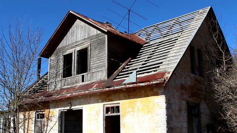 Old brick destroyed house with rusty roof under the blue sky