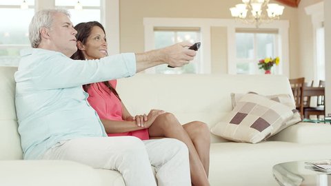 A man turns off the TV with his remote while sitting on the couch with a woman, then they hug