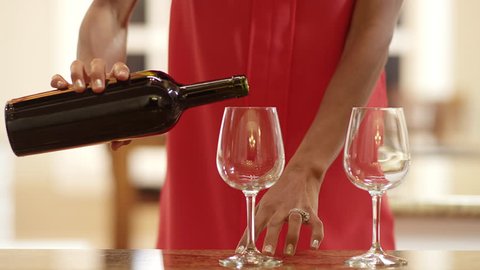 Close up of a woman pouring red wine into two glasses on the counter