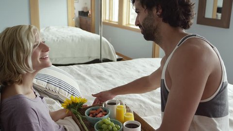 A man brings breakfast in bed to his girlfriend