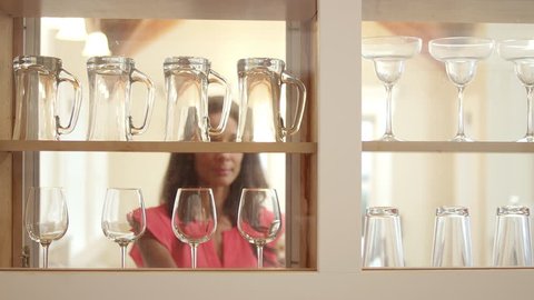 A woman removes wine glasses from the kitchen cabinet