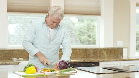 An older man prepares carrots by cutting them on the kitchen counter