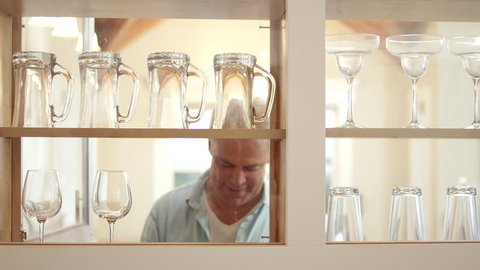 A man removes wine glasses from the kitchen cabinet