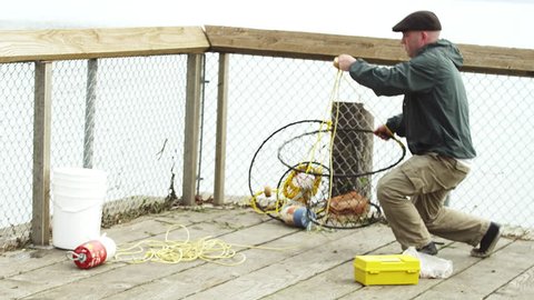 A fisherman standing on a dock picks up his trap and throws it into the water