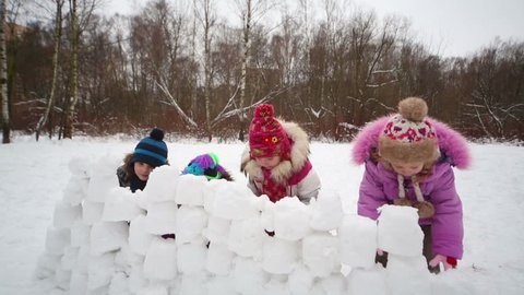 Four children quickly build wall from snow blocks in winter park