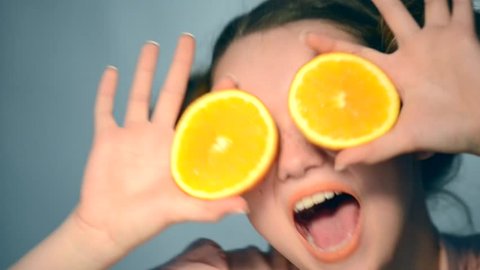 Beauty Model Girl takes Juicy Oranges. Beautiful Joyful teen girl with freckles, funny red hairstyle and yellow makeup. Professional make up. Orange Slices in fast motion. 