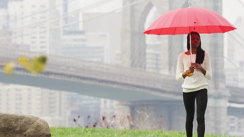 Tilt down of a woman holding an umbrella as she walks away from the Brooklyn Bridge in slow motion