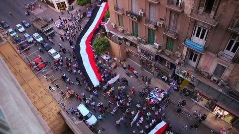 View from overhead looking straight down as protestors carrying banners round a corner and pass through and intersection in the streets of Cairo, Egypt.