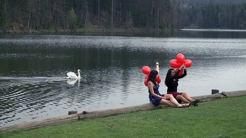Female Friends Enjoying With Red Balloons And Swan in Lake