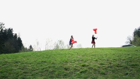 Wide Shot Of Two Women Throwing Red Balloons In To Air In Slow Motion