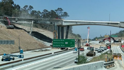 Wide view of heavy equipment tearing down part of a bridge over the 405 freeway in Los Angles.