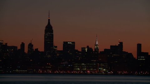 The Empire State Building rises over the skyline of midtown Manhattan under an orange sky during morning twilight in New York City.