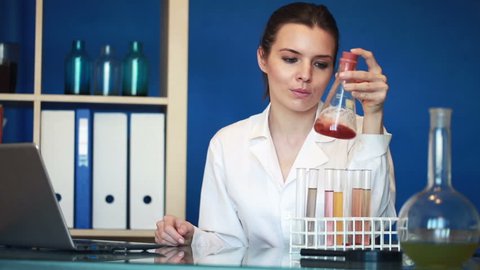 Young female chemist working with laptop and chemicals in lab
