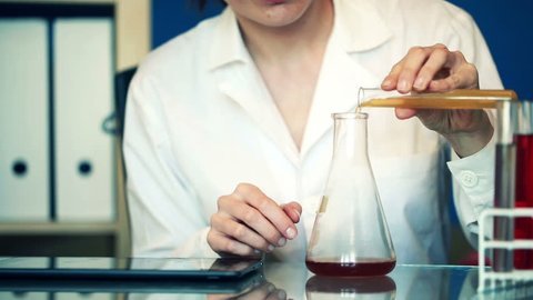 Female scientist with tablet computer and chemicals in erlenmeyer flask
