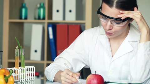 Female biochemist examine apple and writing results in lab
