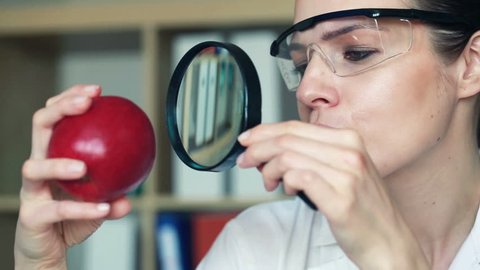 Female biochemist examine apple through magnifying glass in lab
