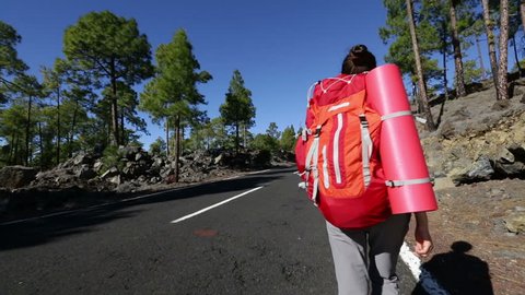 Backpacker traveler walking on road with backpack during holiday travel backpacking. Beautiful outdoors sporty woman model. Tenerife, Canary Islands, Spain.