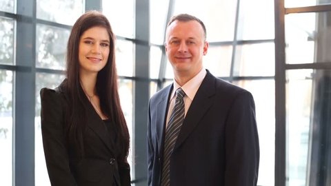 Smiling man and woman in business suits stand near big windows