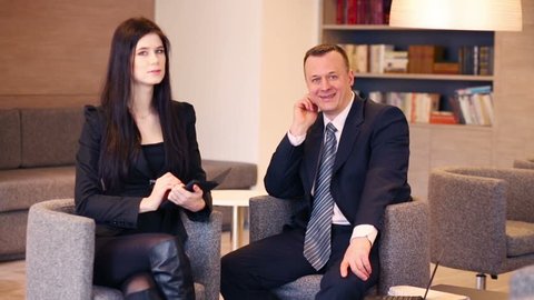 Woman and man in business suit sit on chairs with notepad and talk