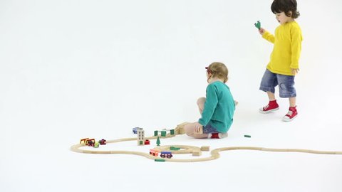 Little pretty boy and girl play with wooden toy railroad in white studio