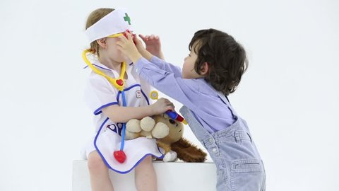 Little boy and girl play with toy medical instruments in white studio