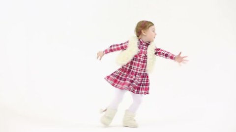 Little girl in fur white vest and boots runs and jumps in white studio