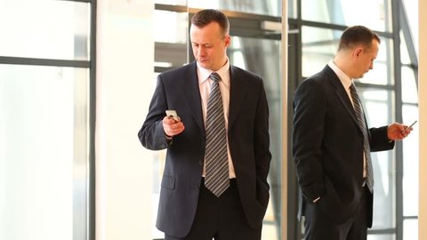Businessman in suit talks by phone near mirror and reflected in it
