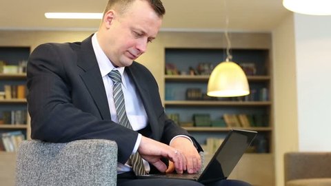 Businessman in suit and tie sits on chair and works with laptop