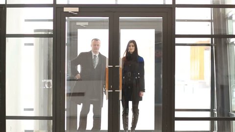 Smiling businessman in suit and woman enter glass door of business center