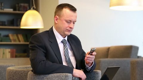 Businessman in suit and tie sits on chair with laptop and phone