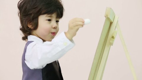 Little handsome boy draws by chalk at chalkboard in studio