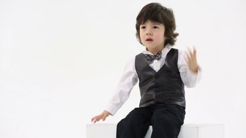 Little cute boy in vest and bow-tie sits and claps hands in white studio