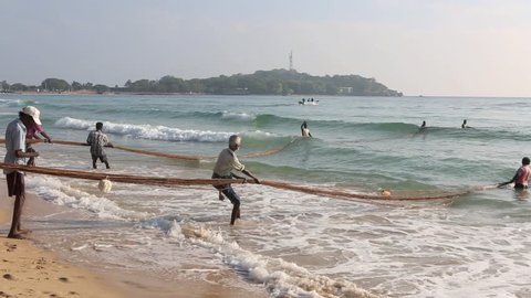 TRINCOMALEE, SRI LANKA - MAR 30: Group of fishermen on beach working together to haul in a large fishing net on March 30, 2014 in Trincomalee, Sri Lanka