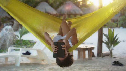 Hispanic woman reading e-book in hammock on caribbean beach at Mahahual, Quintana roo, Mexico