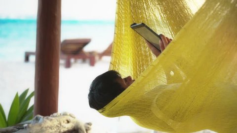 latin woman reading ebook using a electronic tablet in hammock at Mexican Caribbean